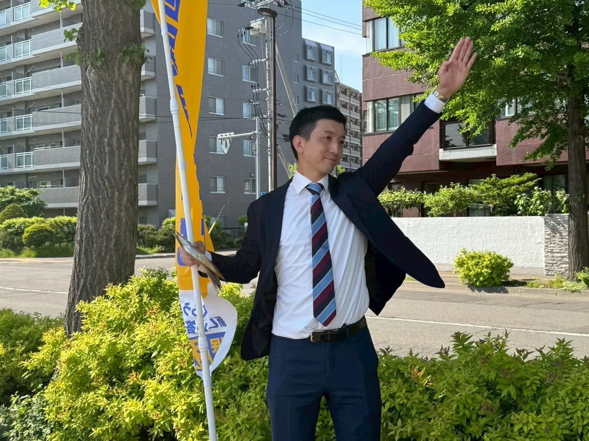 国民民主党の旗の横で手を振る阿部恭介